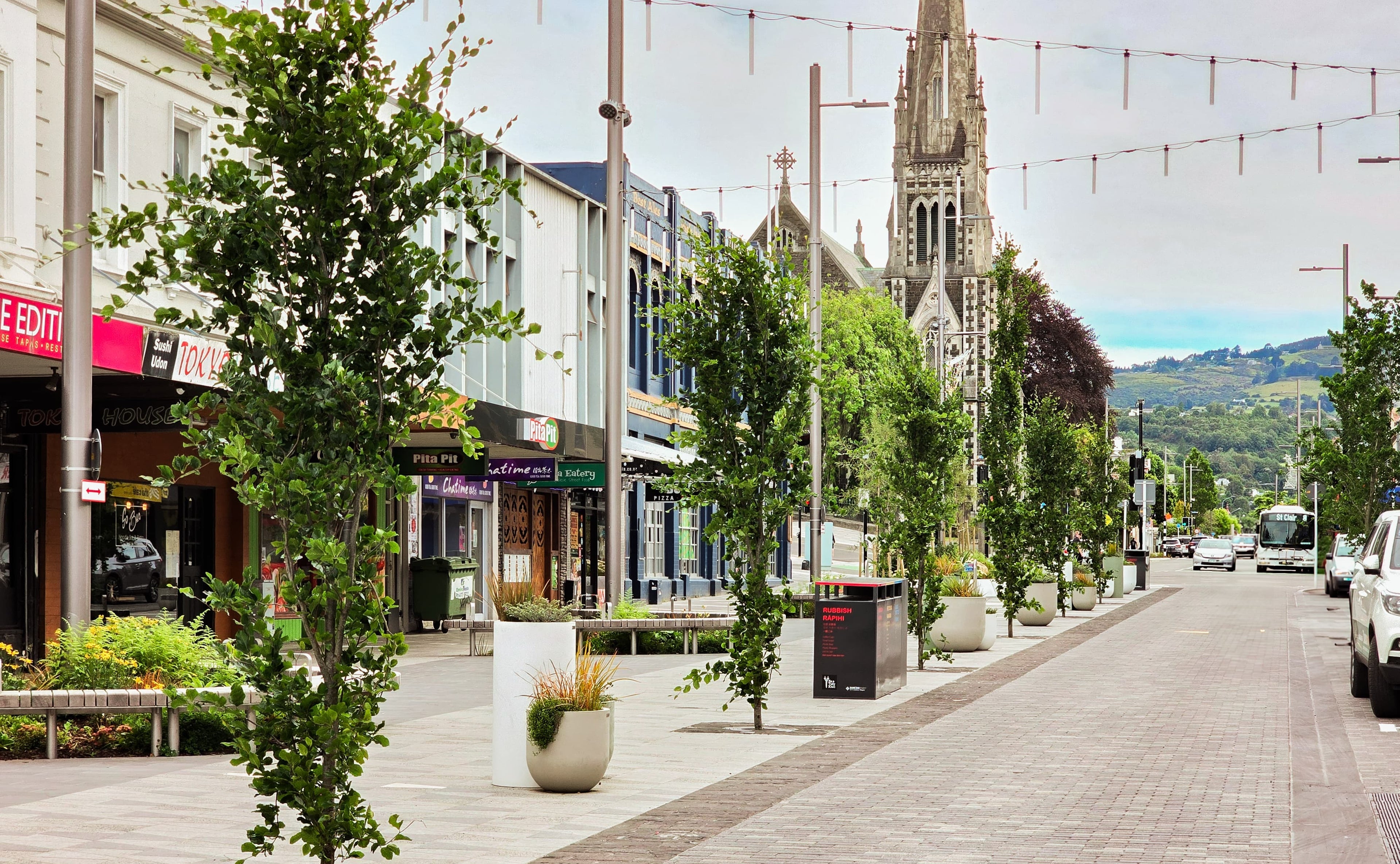 Tall street with trees, buildings, and a church steeple.