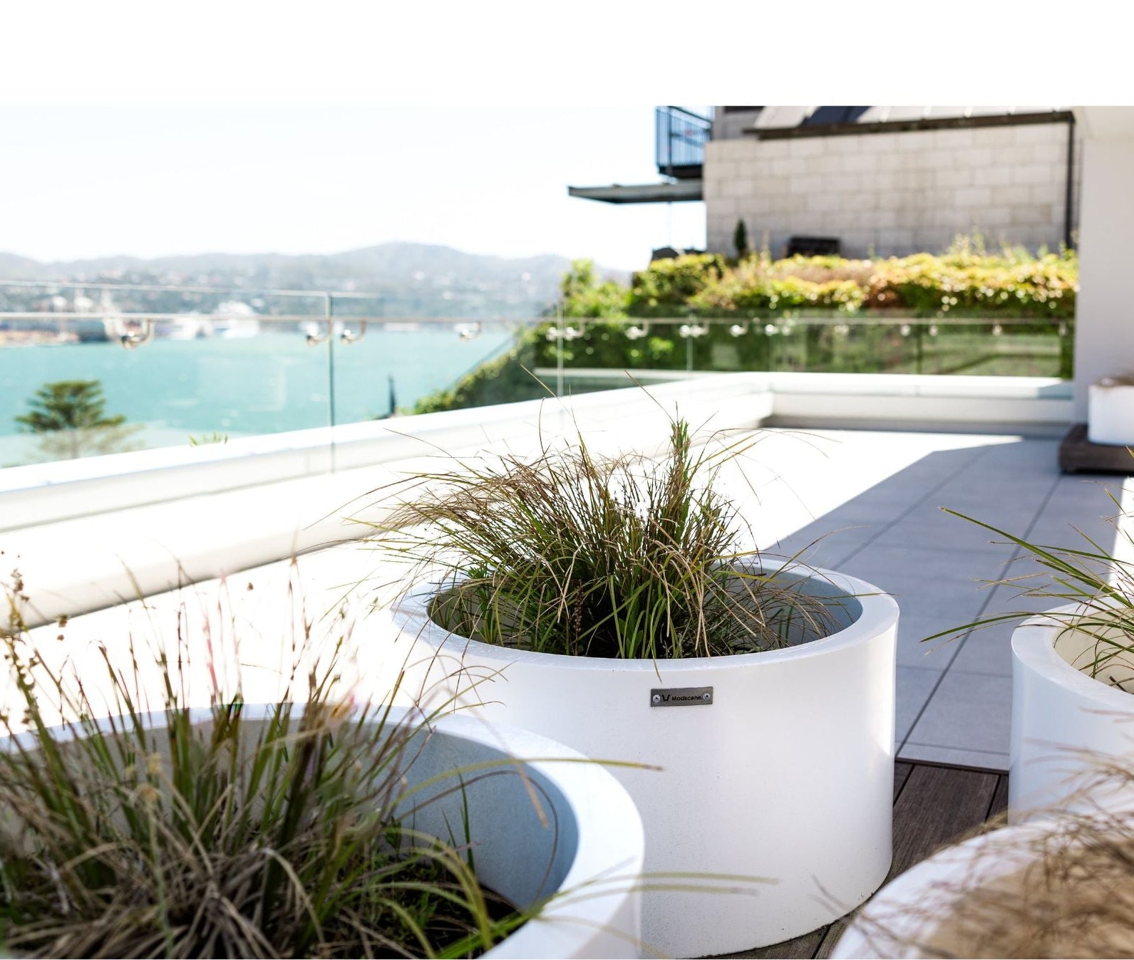 Modern outdoor setting with white planters and a scenic view of water and buildings.