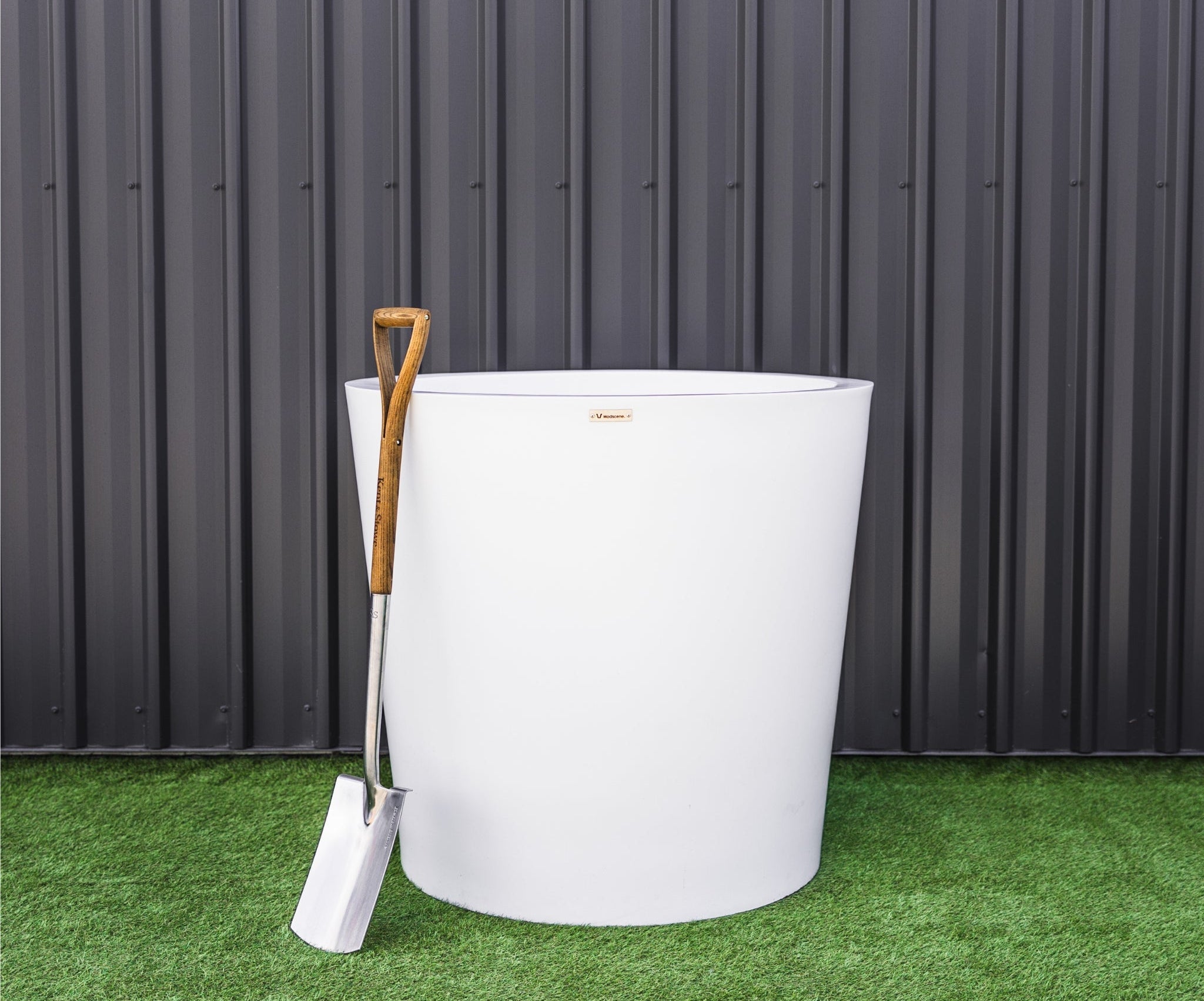 White planter with a wooden shovel against a black metal wall.