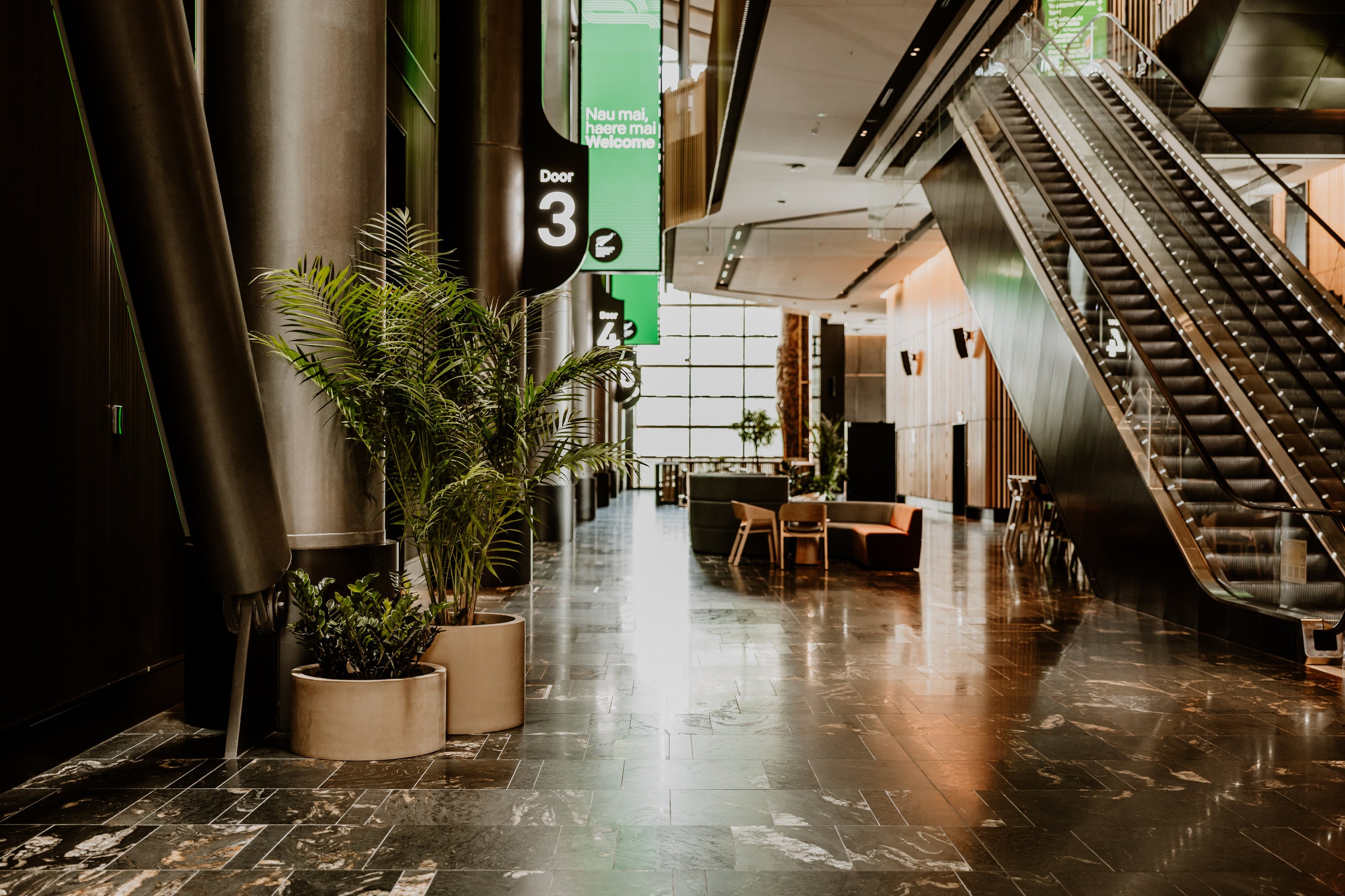 Modern indoor setting with plants, escalator, and seating area.